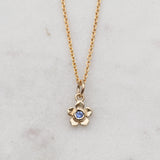 Gold forget me not flower necklace with a blue sapphire