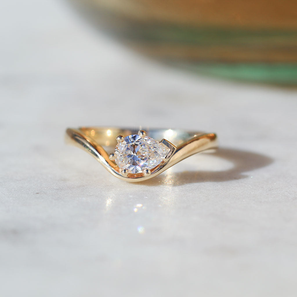 A gold solitaire ring with a pear cut diamond and a curved band