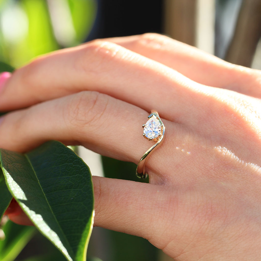 A close-up of a hand wearing a gold ring with a pear-cut diamond