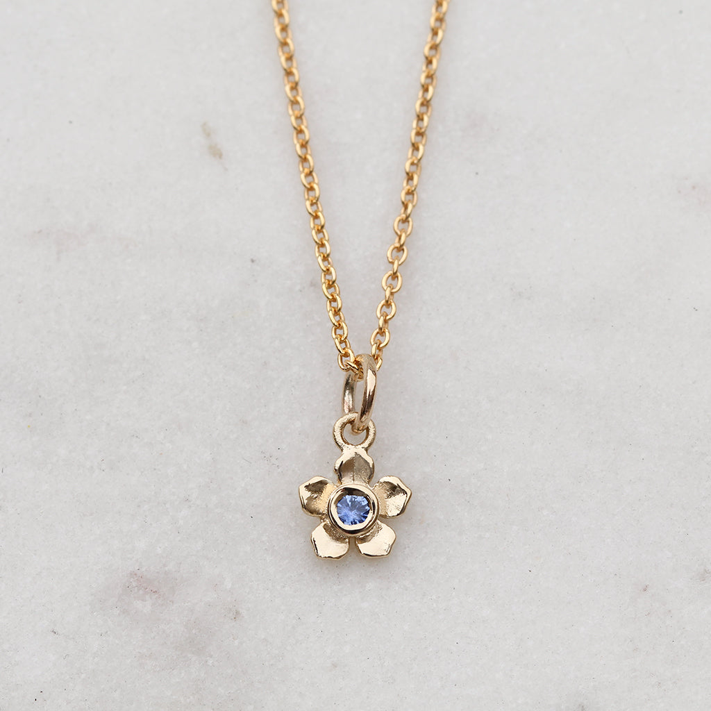 Gold forget me not flower necklace with a blue sapphire