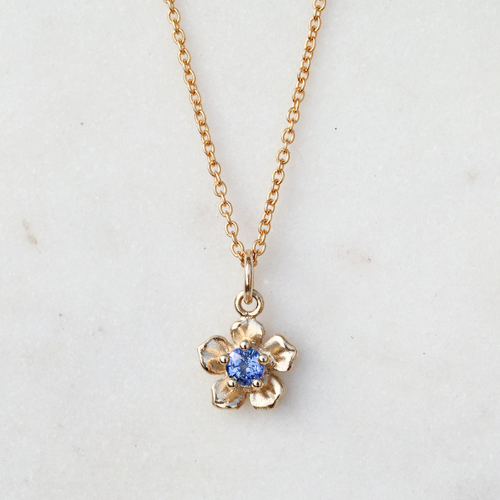gold forget me not flower necklace with a sapphire
