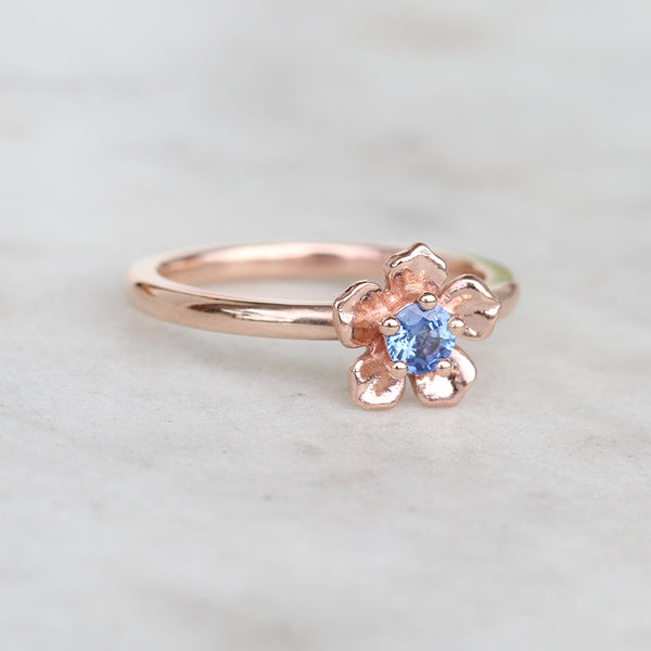 Rose gold forget me not flower engagement ring with a blue sapphire