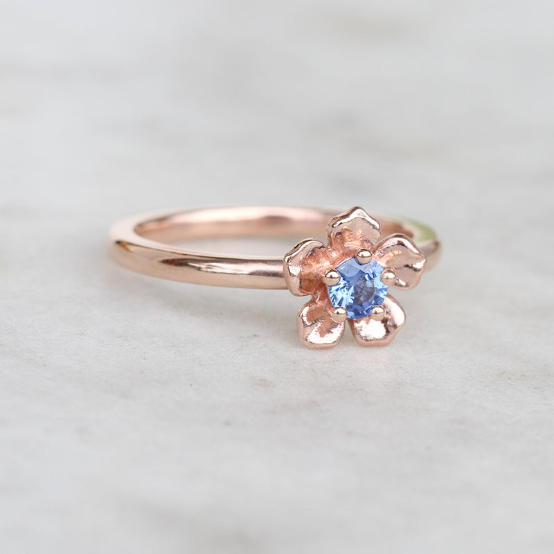 Rose gold forget me not flower engagement ring with a blue sapphire